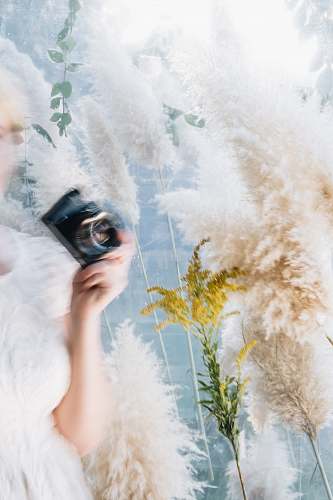 human woman wearing white dress holding black camera plant
