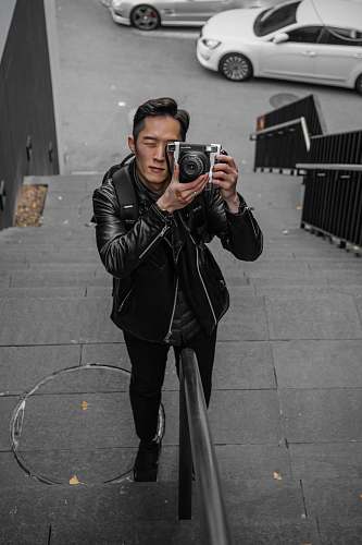 clothing shallow focus photo of man in black leather jacket using camera coat