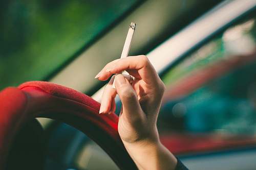smoke selective focus photography of single cigarette stick on person's hand smoking