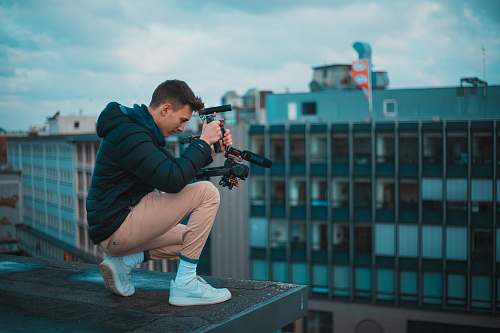 footwear man in black bubble jacket kneeling on top of the building during daytime shoe