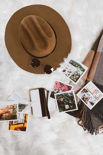 art gold-colored framed sunglasses on brown hat beside white and black leather wristlet surrounded by photos on white and gray floral textile hipster