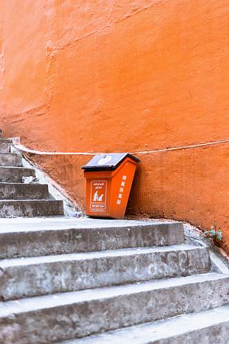 banister orange and black plastic trash bin beside orange painted wall staircase