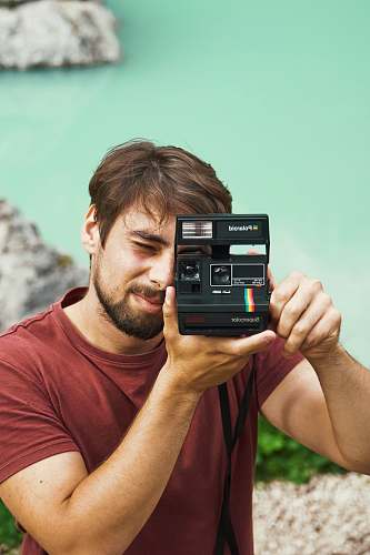 person man wearing maroon crew-neck shirt holding black Instant Polaroid camera photo
