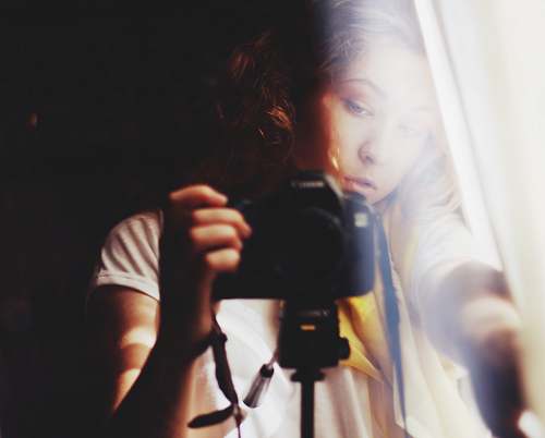 person woman holding DSLR camera beside white curtain photographer