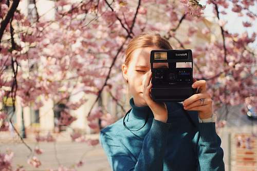 person woman holding Polaroid land camera blossom