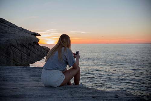 person woman in grey shirts and white sorts sits on rock cliff by the beach photo