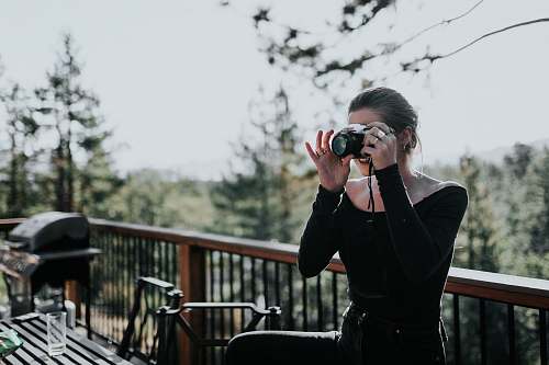 person woman sitting beside balustrade taking photo electronics