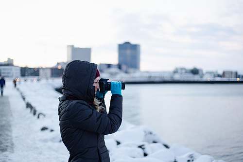 person woman wearing black hooded jacket using DSLR camera photographer