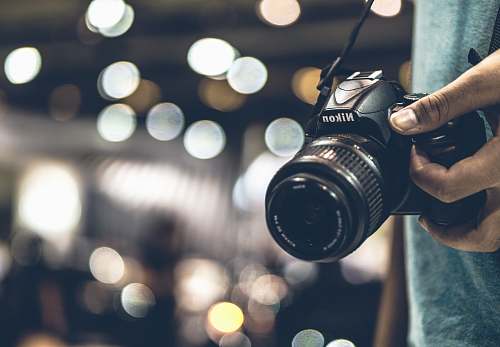 camera bokeh photography of person holding Nikon DSLR camera with strap electronics