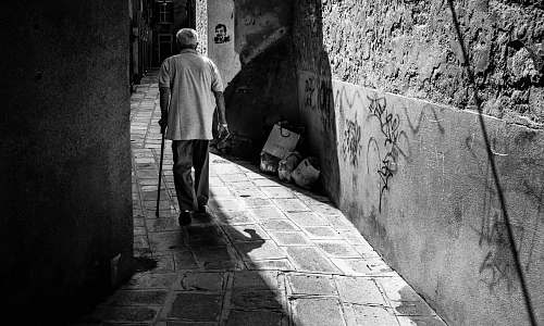 people grayscale photography of man holding cane black-and-white
