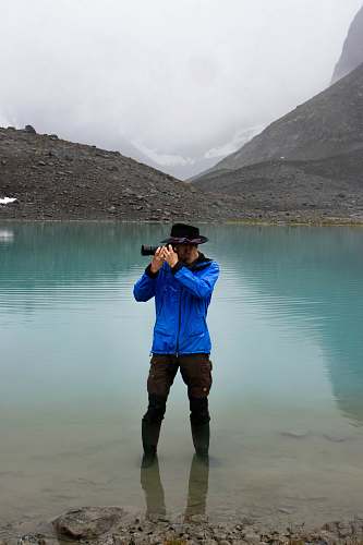 human man standing on body of water using DSLR camera apparel