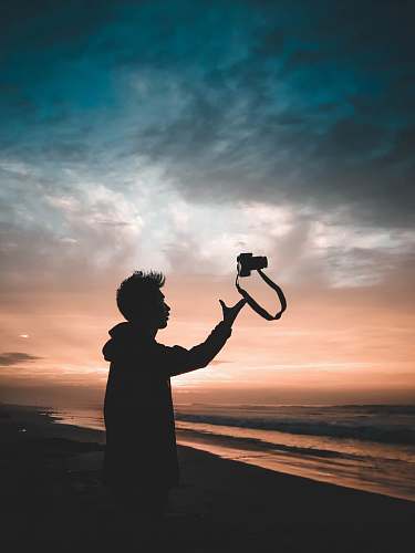 human man throwing camera standing near shore during sunset photographer