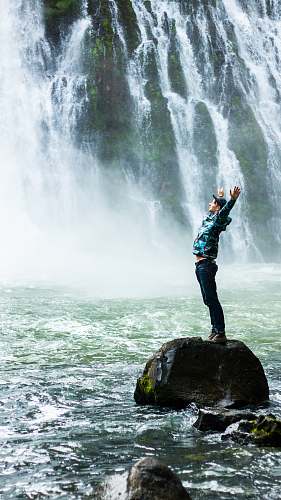 nature man standing on black rock surrounded body of water rock