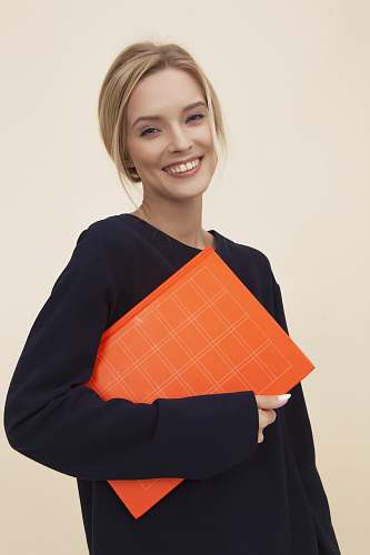 apparel smiling woman standing while holding orange folder sleeve