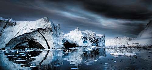 glacier snow capped mountain near body of water under gray clouds outdoors