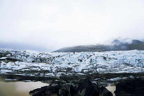 glacier snow covered rocky field near body of water during daytime snow