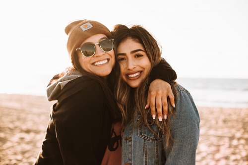 human woman hugging other woman while smiling at beach person