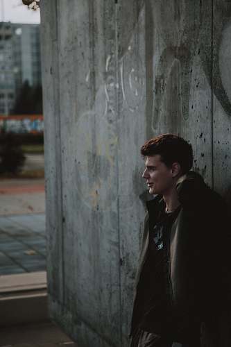 clothing man wearing jacket leaning on wooden wall during daytime man