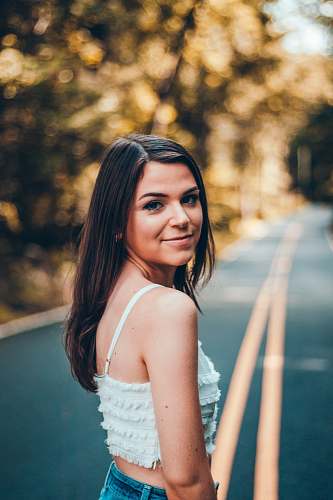 clothing selective focus photography of woman standing on road between trees fashion