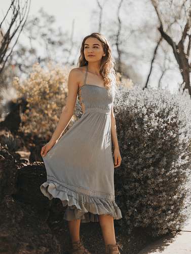 clothing woman in gray spaghetti strap dress standing near flower and smiling gown