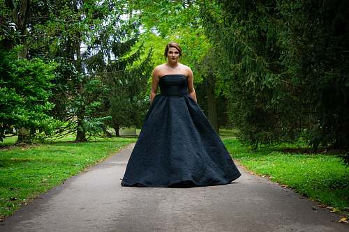 clothing woman wearing black sweetheart dress walking on asphalt pathway evening dress