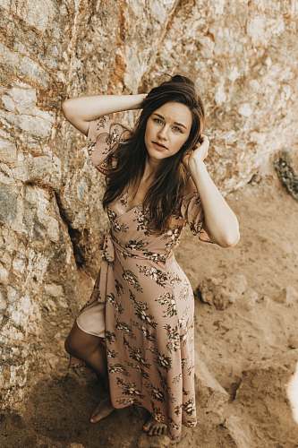 apparel woman in brown and white floral short-sleeved dress standing near rock during daytime gown