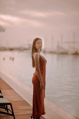 apparel woman wearing orange sleeveless dress standing near body of water during daytime evening dress