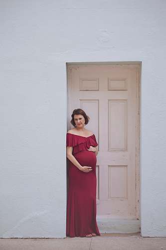 apparel woman wearing red off-shoulder maxi dress leaning on white door door
