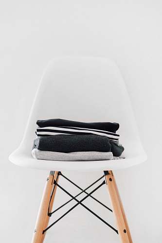 interior pile of black, white, and gray textiles on white padded chair with brown frame furniture