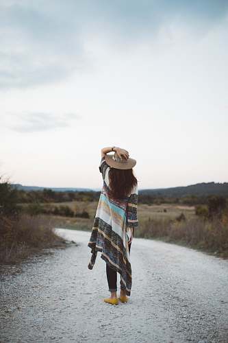 people standing woman holding her hat at the middle of the road during day woman