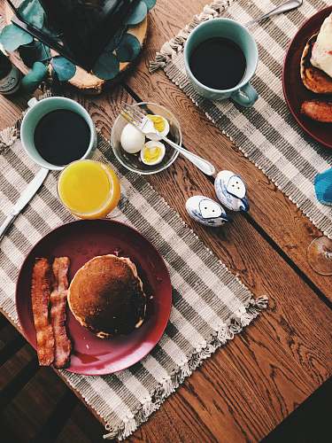 breakfast baked bread on round red ceramic plate near glass of orange juice, cup of coffee, and boiled eggs meal