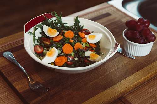 vegetable bowl of salad with slide of cooked egg with grapes on the side plate