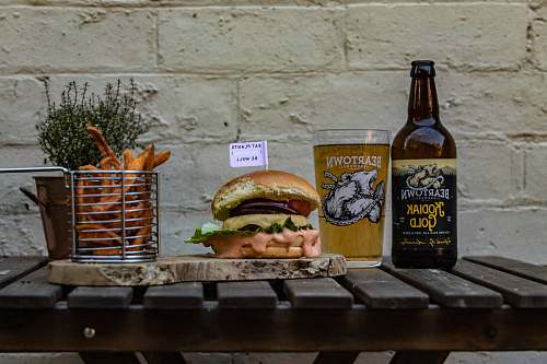 burger hamburger on chopping board by basket of fries and beer bottle alcohol