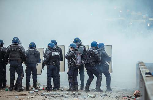 person riot police holding shield in front of smoke apparel