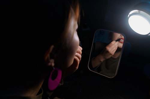 person woman facing the mirror putting lipstick on the lips hand