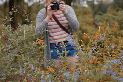 person woman holding camera standing beside flowers during daytime camera