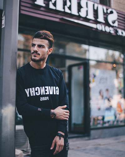 person man in black Givenchy sweatshirt standing beside of post in front of Strek store during daytime shallow focus photography human