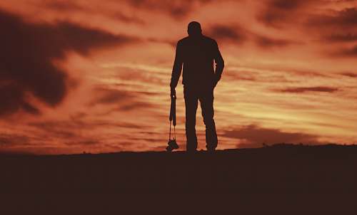 person standing man carrying camera facing the field during day silhouette
