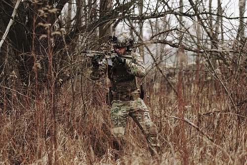 military man holding assault riffle beside bare tree military uniform
