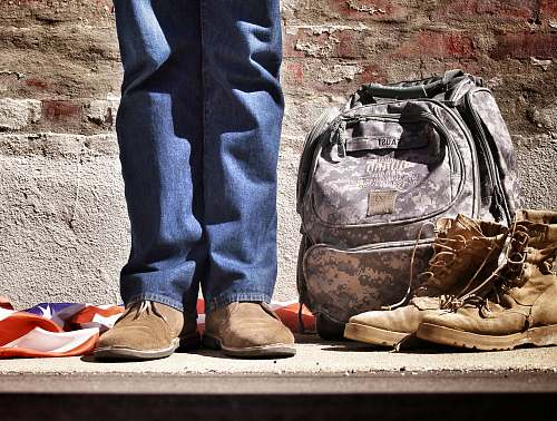 footwear minimalist photography of person standing near backpack and boots shoe