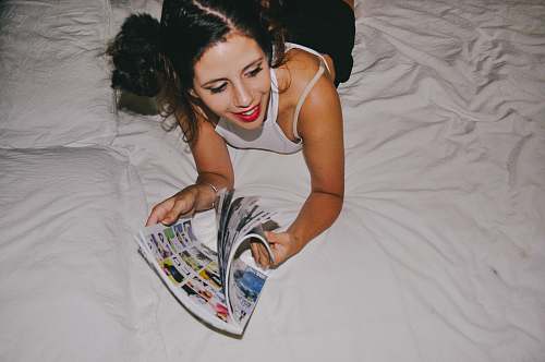 human smiling woman lying on bed while reading magazine bed
