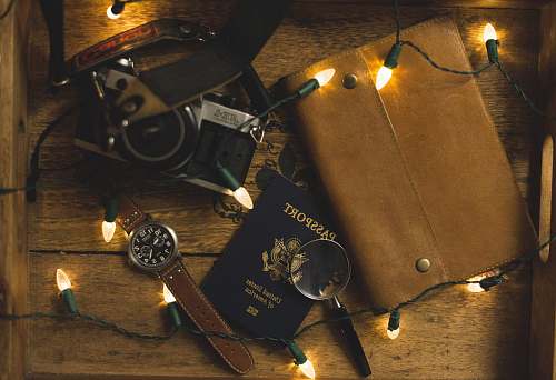 brown passport and SLR camera on table with string lights lights