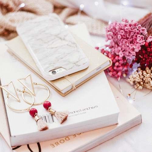 pink iPhone on book beside gold-colored earrings girly