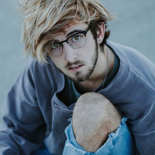 a man with blonde hair and glasses sitting on the ground