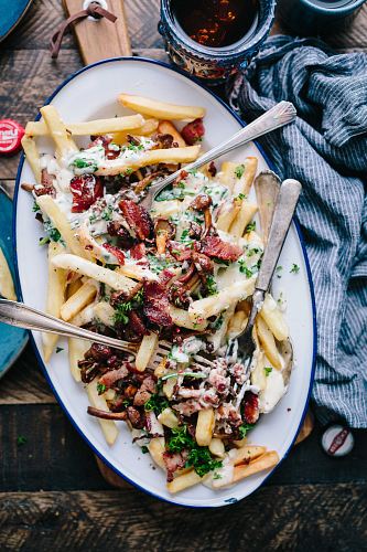 bacon strips and melted cheese topped fries on oval white and blue platter with gray stainless steel forks