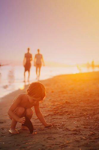 boy playing sand on seashore during sunset