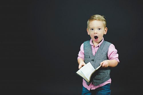boy wearing gray vest and pink dress shirt holding book