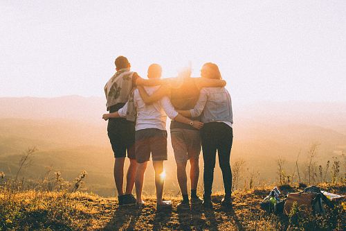 four person hands wrap around shoulders while looking at sunset