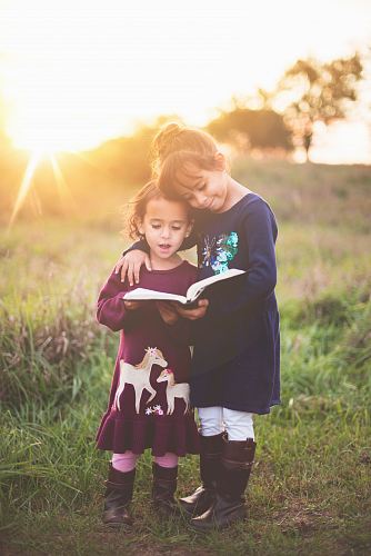 girl's left hand wrap around toddler while reading book during golden hour