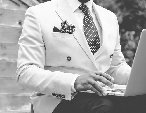 grayscale photo of man wearing suit jacket using laptop